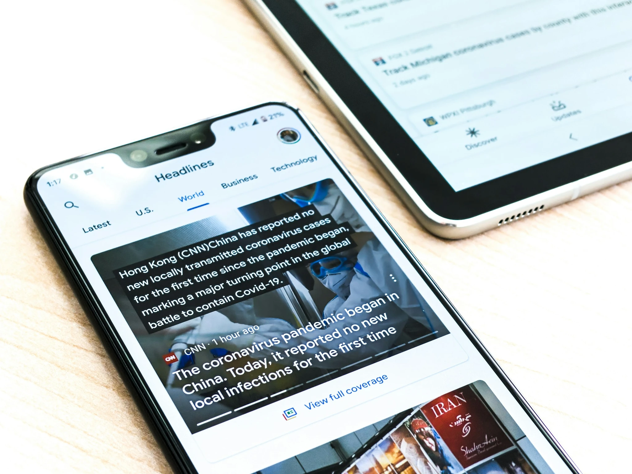 A Google pixel 3XL showing Covid-19 information from the Google News app sits on a wooden table next to a Samsung Galaxy Tablet.